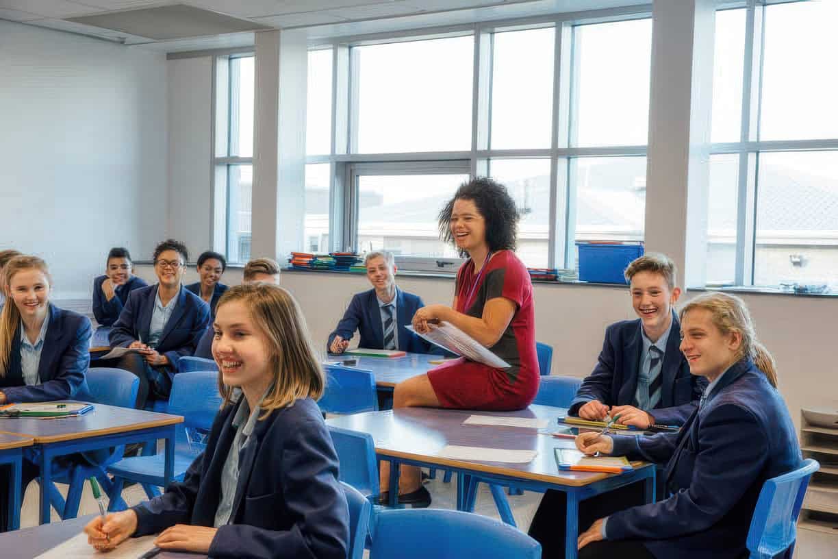 Teacher leading discussion with smiling students in classroom.