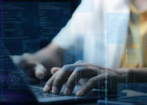 Hands typing on laptop with digital code overlay.