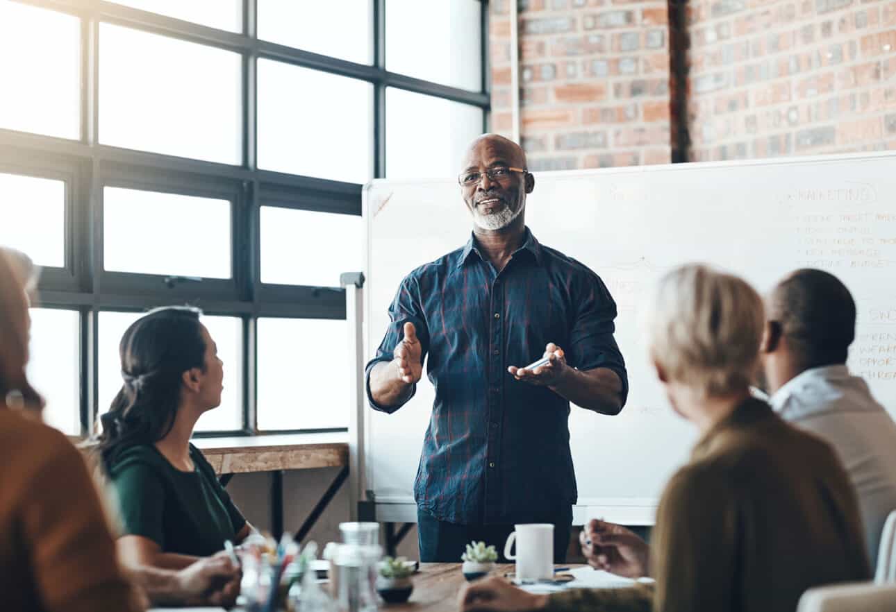 Man presenting to colleagues in a meeting room.