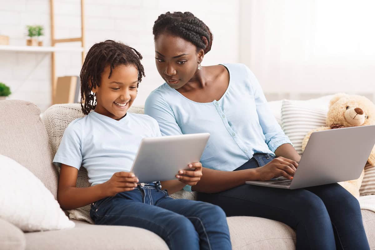 Smiling woman and child using devices on sofa.