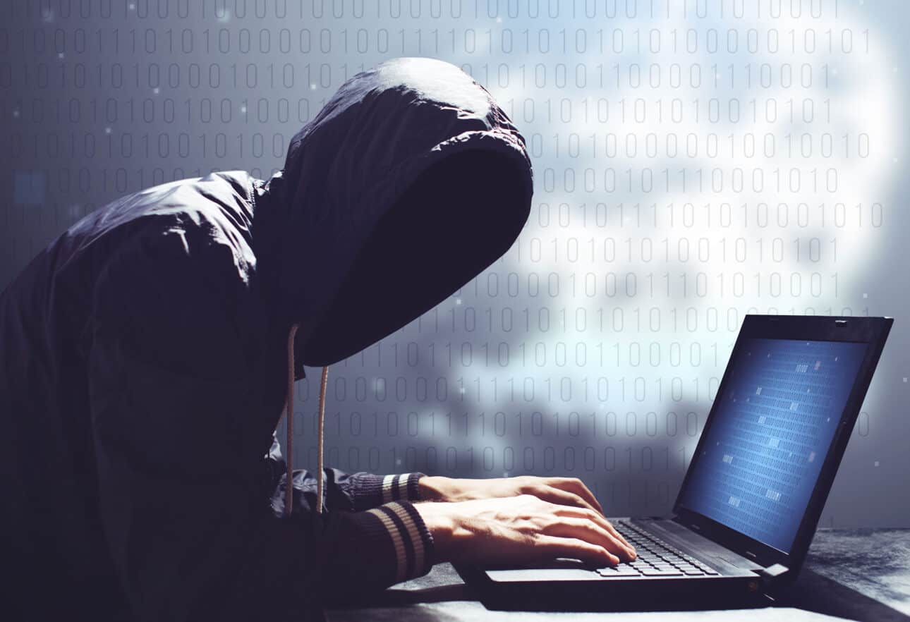 Hacker in hoodie using laptop for cyber activities.