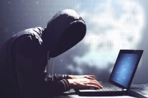 Hacker in hoodie using laptop for cyber activities.