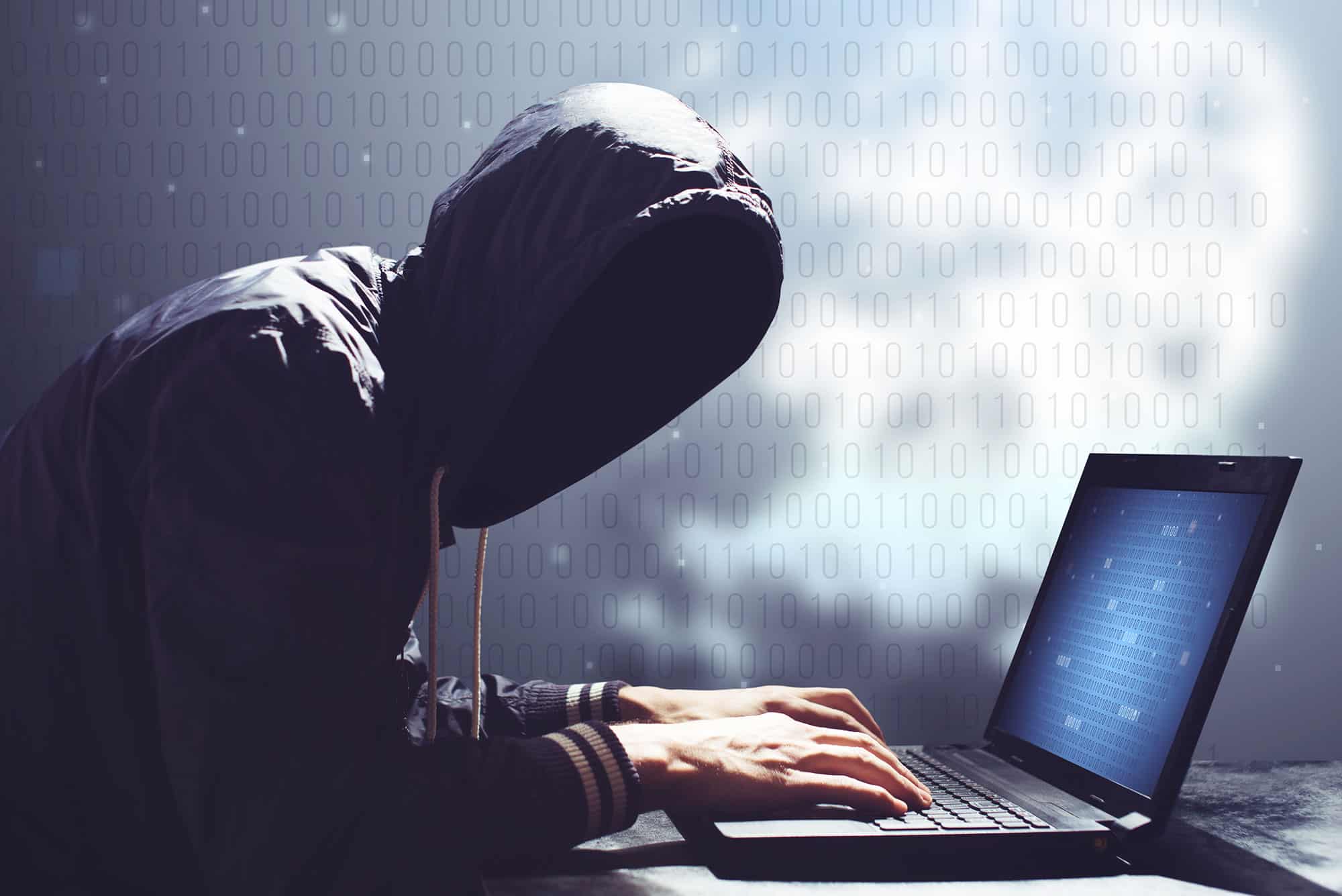 Hacker in hoodie using laptop for cyber activities.