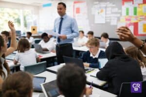 Teacher in classroom with students working on laptops.