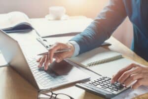 Person using laptop and calculator at desk